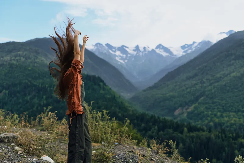 A person stands on a rocky overlook in a vast mountain landscape with arms raised, embracing freedom and adventure, capturing a triumphant moment and a strong connection with nature