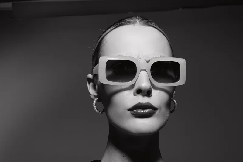 Portrait of a fair skinned Caucasian woman wearing large sunglasses and hoop earrings in monochrome studio. Fashion, style, and modern elegance concept.