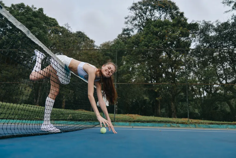 Young female tennis player in action on a blue court, wearing sporty attire, showcasing joy and determination amidst a vibrant green background