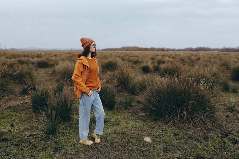 Woman lifestyle outdoors in a grassy field, wearing straw hat, yellow jacket and denim pants, calm pose in golden autumn light, candid lifestyle portrait