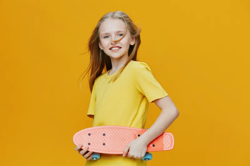 Happy girl with a skateboard in a yellow outfit against a vibrant yellow background, showcasing a cheerful expression and playful summer vibes