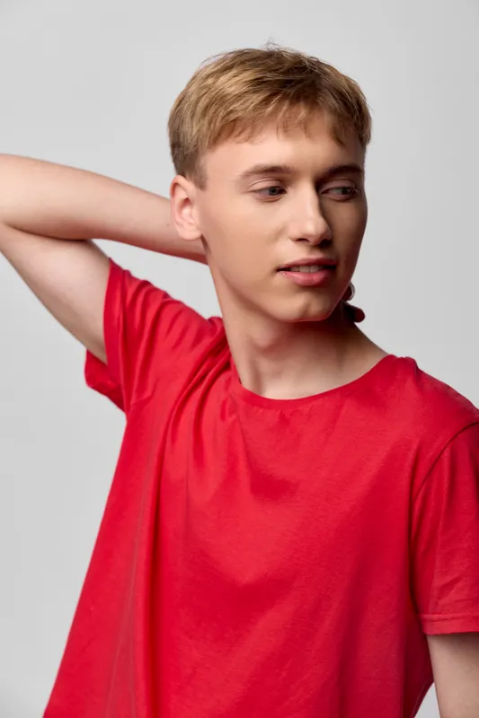 Casual young man in a red t shirt adjusting his neck with a relaxed pose, soft studio lighting, simple background, contemporary lifestyle image suitable for fashion and wellbeing topics