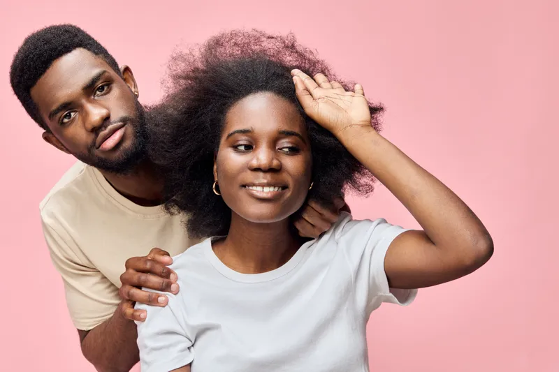 Happy young Black couple with natural hair on a pink background celebrating their love, showcasing emotions through expressive poses and casual outfits