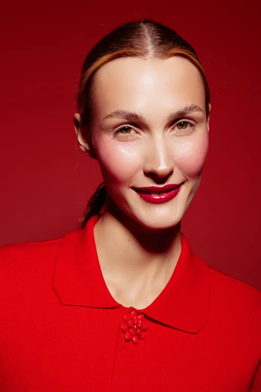 Portrait of a smiling woman with red lipstick and blush wearing a red top against a red background. Concept of beauty, fashion, makeup, and confident expression in studio lighting.