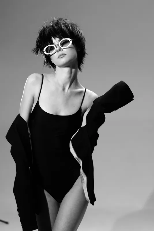 Black and white portrait of a fashionable young woman wearing sunglasses and a swimsuit with a jacket.
