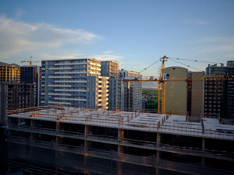 Construction crane and building apartment highrise with scaffolding in city skyline at sunset, concrete floors and tower cranes on an active residential development site showing urban progress.