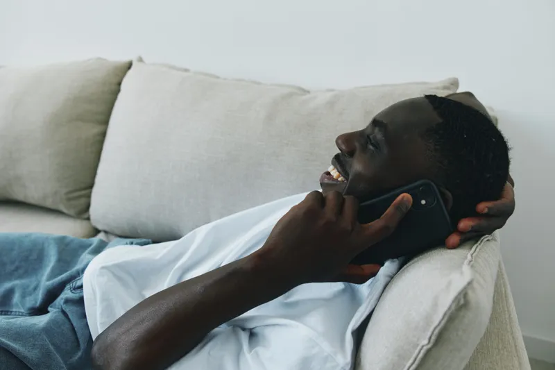 Happy Black man talking on the phone while relaxing on a couch in a modern home Casual attire and smiling expression create a positive vibe