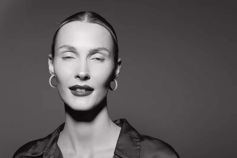 Portrait of a Caucasian woman with pale skin and slicked back hair wearing hoop earrings and dark lipstick in a studio. Concept of elegance, fashion, and beauty with monochrome lighting.