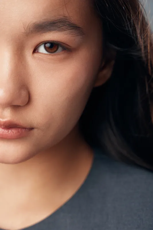 Closeup of young woman face with natural skin tone and dark hair looking at camera, portrait with serious expression and soft lighting on neutral background.