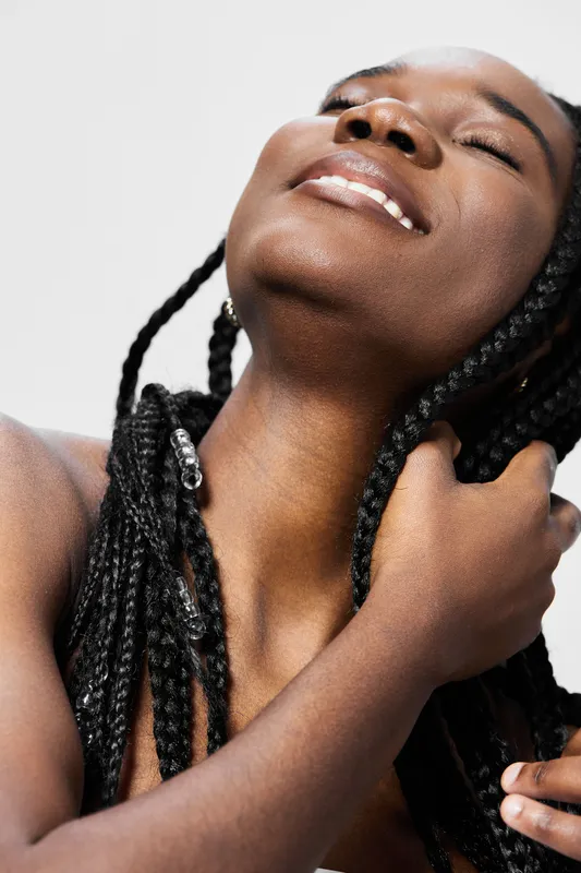 Beautiful young woman with braided hair expressing joy and self love against a light background, ideal for wellness and beauty themes