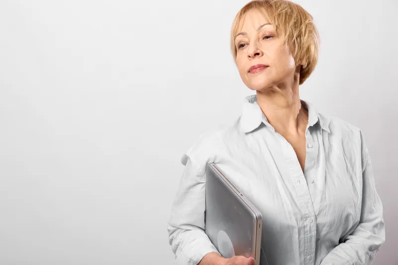 Woman doctor stressed by burnout holds tablet, signaling elderly mental health concern in bright clinic. Tired serious expression shows healthcare stress.