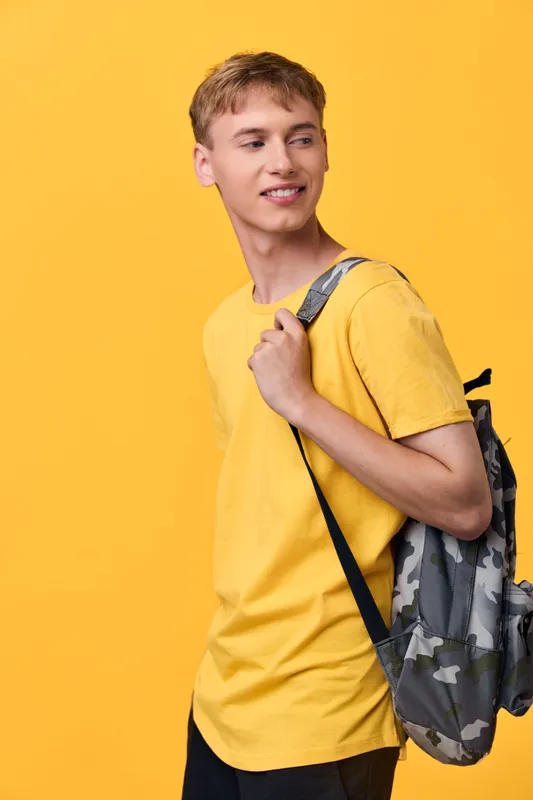 Young traveler with a backpack stands against a bright yellow backdrop, ready for adventure, casual fashion and sunny vibe, exploring daily life and optimism in a cheerful pose