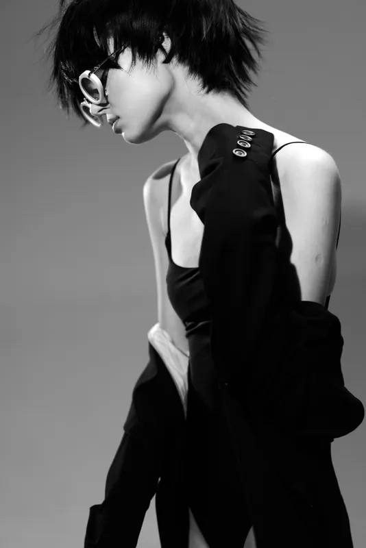 Stylish woman with short hair wearing sunglasses and dark clothing in black and white urban setting.