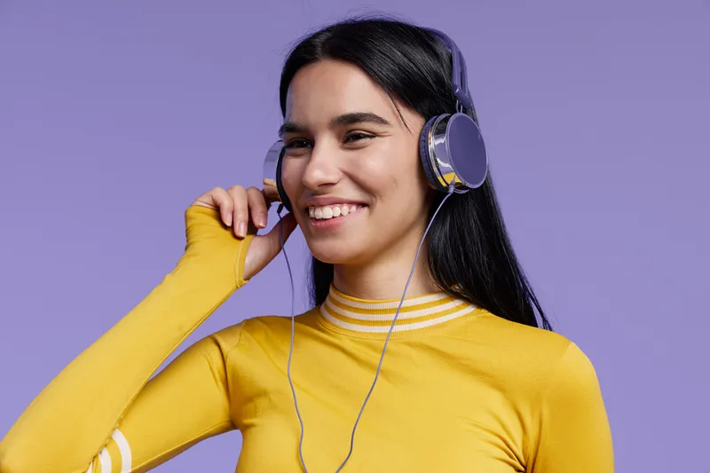 Active woman sport fitness listening to music with headphones smiling, wearing yellow sweater against purple background, youthful healthy lifestyle concept.
