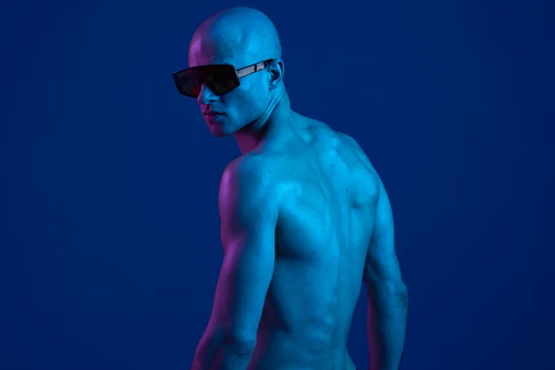 A striking blue-toned image of a confident man showcasing his back, wearing sunglasses and illuminated against a vibrant background. Captivating and modern.