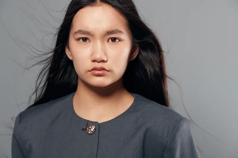 Portrait of serious woman with long hair wearing gray clothing studio shot with soft lighting isolated on neutral background looking at camera with calm expression and natural makeup.