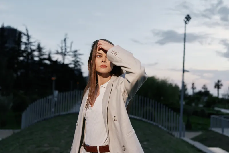 Confident businesswoman in a stylish outfit, standing outdoors against a sunset backdrop, conveying determination and professionalism in urban setting.