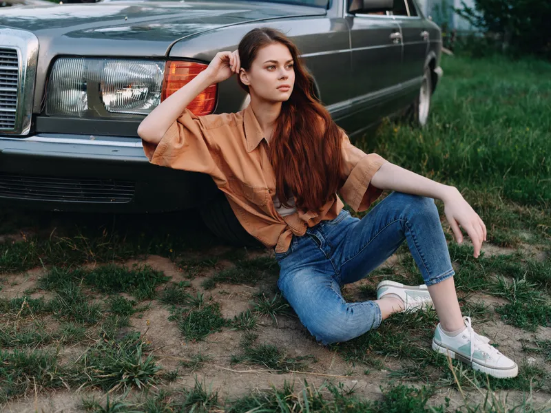 Young woman with long hair in casual style posing next to a vintage car, showcasing relaxed emotions and a natural setting, perfect for lifestyle photography.