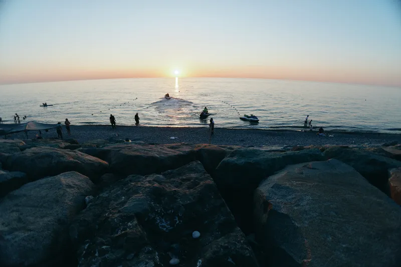 fishermen at sunset, sea horizon, peaceful water, coastal rocks, calm evening, boating activity
