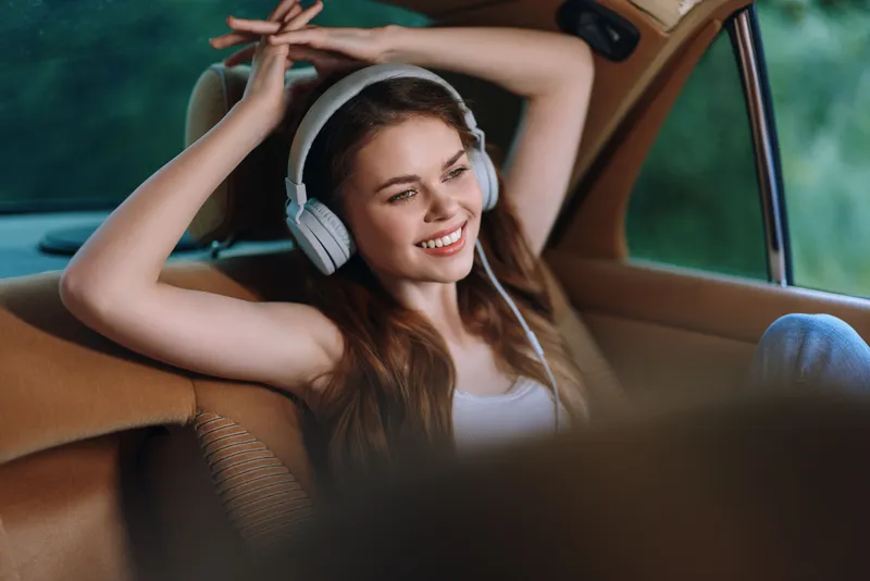 Happy young woman enjoying music with headphones in a vintage car interior, relaxed atmosphere, soft colors, ideal for lifestyle and travel concepts.