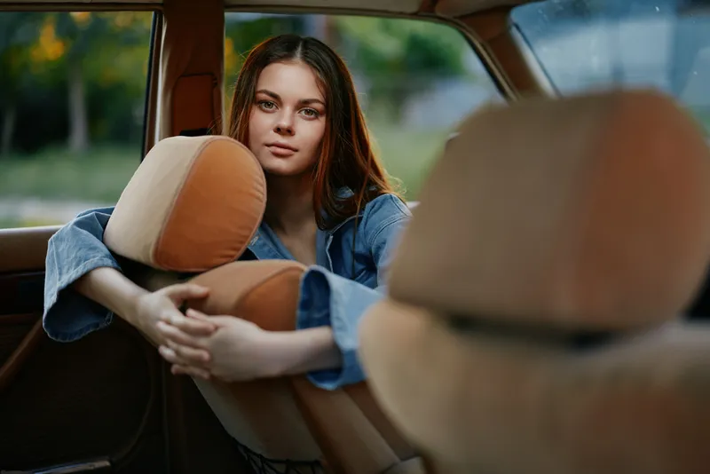 Young woman relaxing in a car, showcasing casual style, serene expression, and warm tones, perfect for lifestyle photography and concepts of freedom and travel.