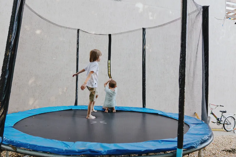 Happy children jumping on a trampoline, enjoying outdoor play in a sunny environment. Perfect for illustrating summer fun and childhood joy. ###