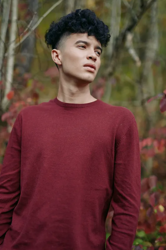 A candid portrait of a young man in a burgundy sweater amid autumn foliage, conveying authenticity and credibility through relaxed pose and natural light.