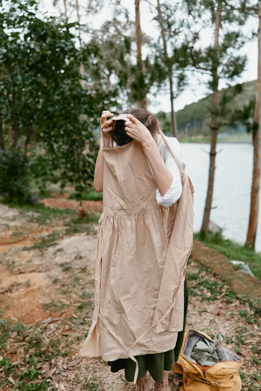 Young woman holding a dress while standing by a serene lake in a natural environment, showcasing a relaxed, earthy style and an emotional connection to nature