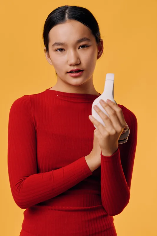 Young woman in red sweater holding white headphones on bright background, looking at camera, technology device, music listening, modern lifestyle and casual style portrait.