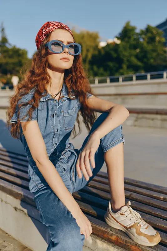 Lifestyle woman in modern boho-western denim street style wearing blue sunglasses and red bandana with natural curls in warm film color background outdoors.