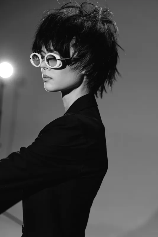 Black and white portrait of a stylish woman wearing round sunglasses and a dark jacket