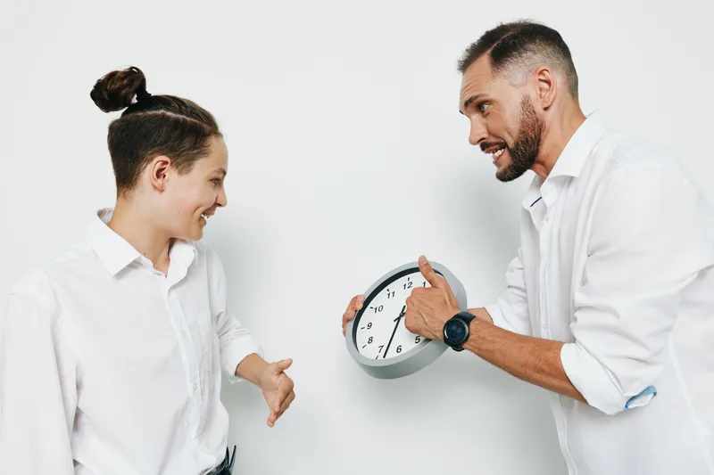 A business professional man shares a light moment with a colleague against a plain colored background, conveying confidence, teamwork, and positive energy.