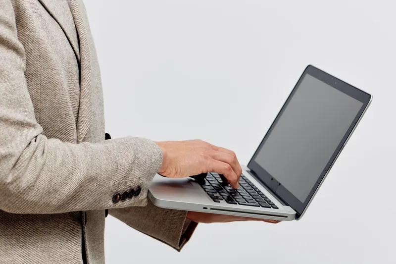 man working with laptop in beige jacket typing on keyboard isolated plain background digital nomad concept