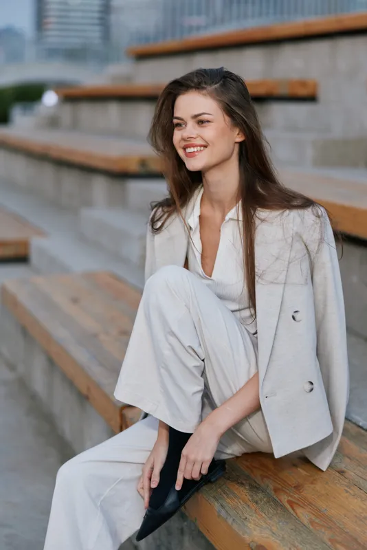 Confident woman in business attire smiling outdoors, showcasing modern business fashion in a bright urban setting.