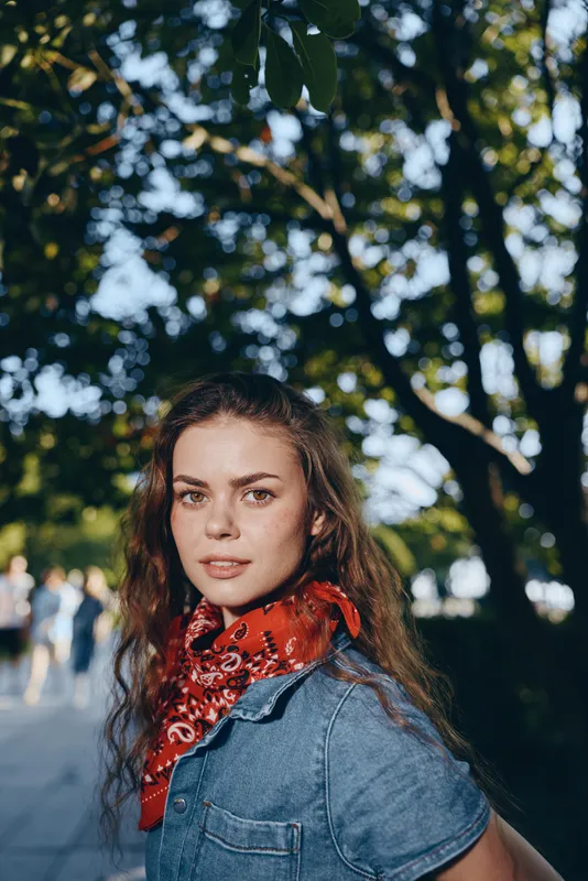 Lifestyle woman in modern boho-western denim street style with red bandana, natural light and film color creating warm and relaxed outdoor atmosphere.