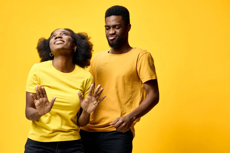 Happy African American couple dancing in bright yellow clothing against a vibrant yellow background, expressing joy and carefree emotions