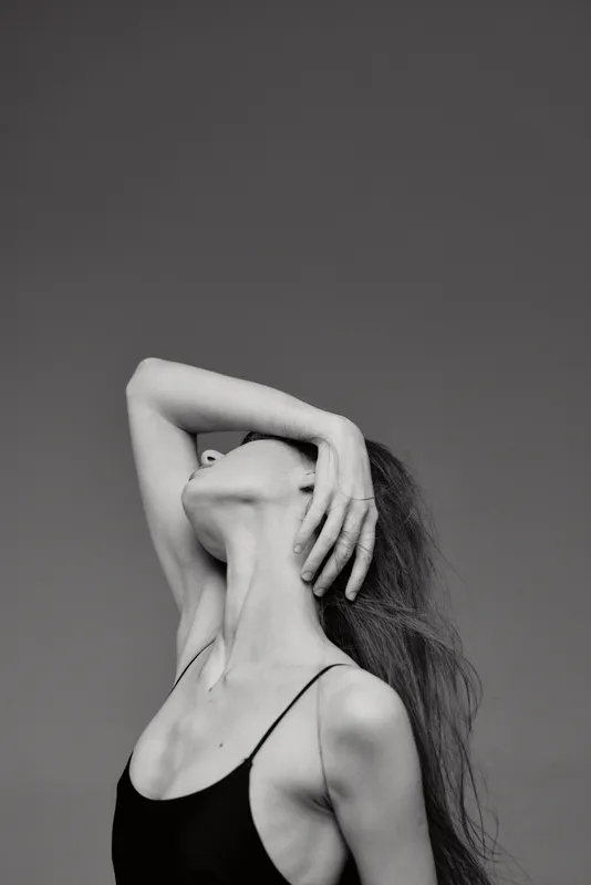 Black and white artistic portrait of a slender woman with long hair posing gracefully against a plain background.
