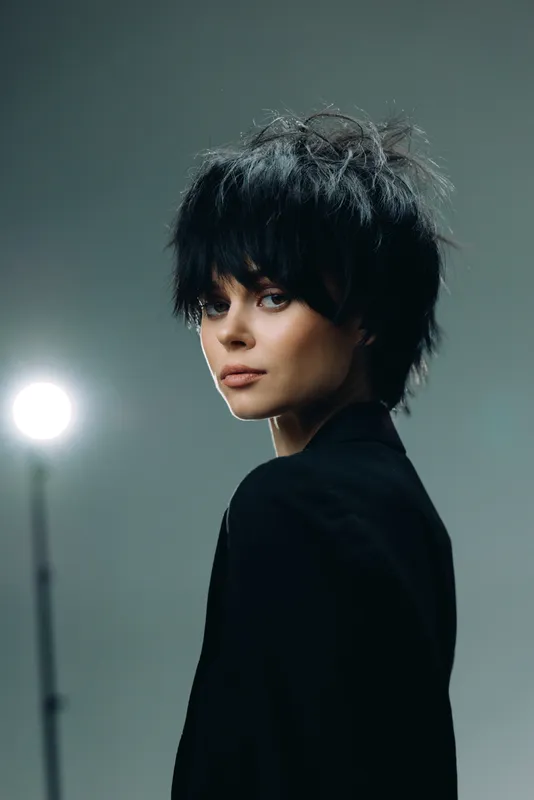 Portrait of stylish woman with short black hair in dark clothing, moody lighting, and neutral background