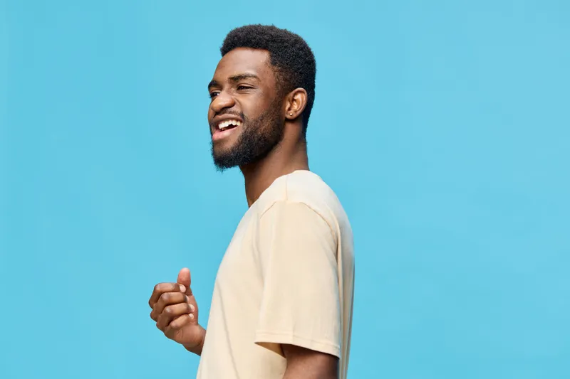 Happy African man smiling against a blue background, wearing a casual beige t shirt, displaying confidence and joy, perfect for concepts related to positivity and self esteem