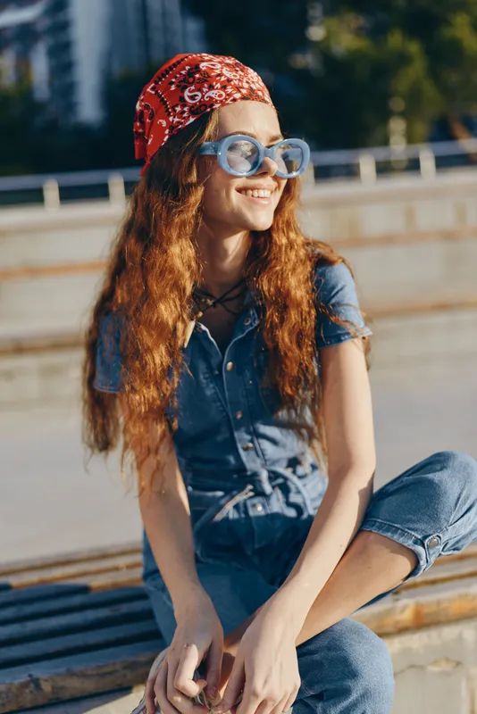 lifestyle woman in modern boho-western denim street style with red bandana and sunglasses, smiling outdoors in warm film color sunlight, casual urban vibe