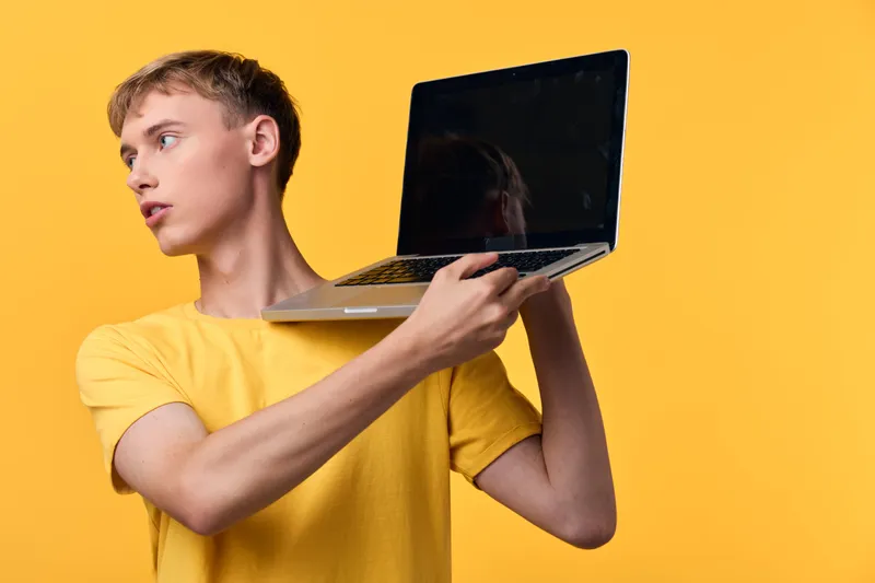 Laptop, man, yellow background, holding, technology, device, presentation, casual, fashion in studio, a focused youth lifts a laptop to the side, signaling digital work, online learning and creative