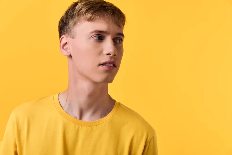 Young man in a bright yellow t shirt stands before a yellow studio backdrop, casual fashion vibe, contemplative gaze, clean composition ideal for lifestyle branding and creative campaigns.