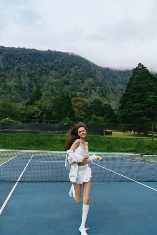 Happy young model in sportswear running on a tennis court with lush green hills in the background perfect for fitness and outdoor sports concepts