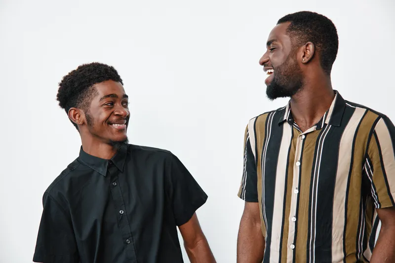 Two African American men smiling and looking at each other in casual shirts on white background. Young black males with dark skin and happy expressions in studio.