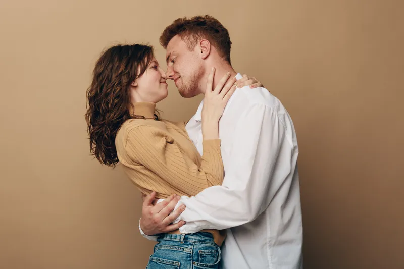 Young couple embraces closely with eyes closed, smiling gently in a warm beige studio. Concept of love, intimacy, affection, and romantic connection between partners.