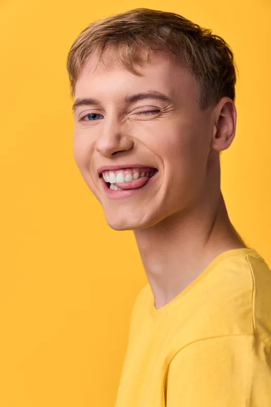 Smiling and wink in a yellow shirt against a solid yellow background, conveying playful energy, casual style, and upbeat mood ideal for lifestyle, fashion, or marketing campaigns.