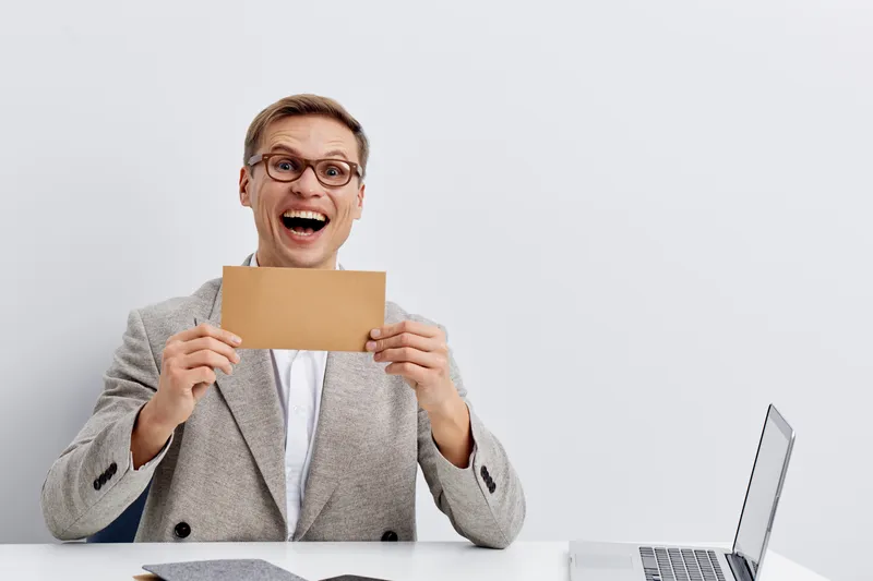 cheerful man holding envelope surprised expression sitting at laptop digital nomad remote work concept