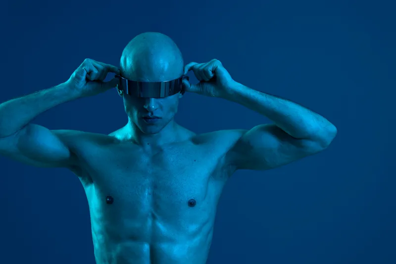 Futuristic man with virtual reality headset in blue lighting, showcasing high-tech innovation and modern lifestyle, emphasizing the integration of technology into daily life.