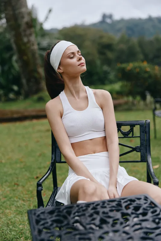 Young woman enjoying a moment of relaxation in sportswear outdoors, embodying tranquility and health with a peaceful expression in a lush garden