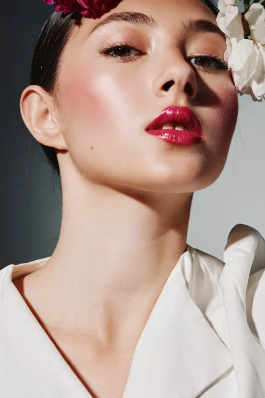 Close-up of a woman with glossy red lips and natural skin glow wearing delicate floral hairpieces. Creative fashion beauty portrait with soft lighting emphasizing elegance and skincare.